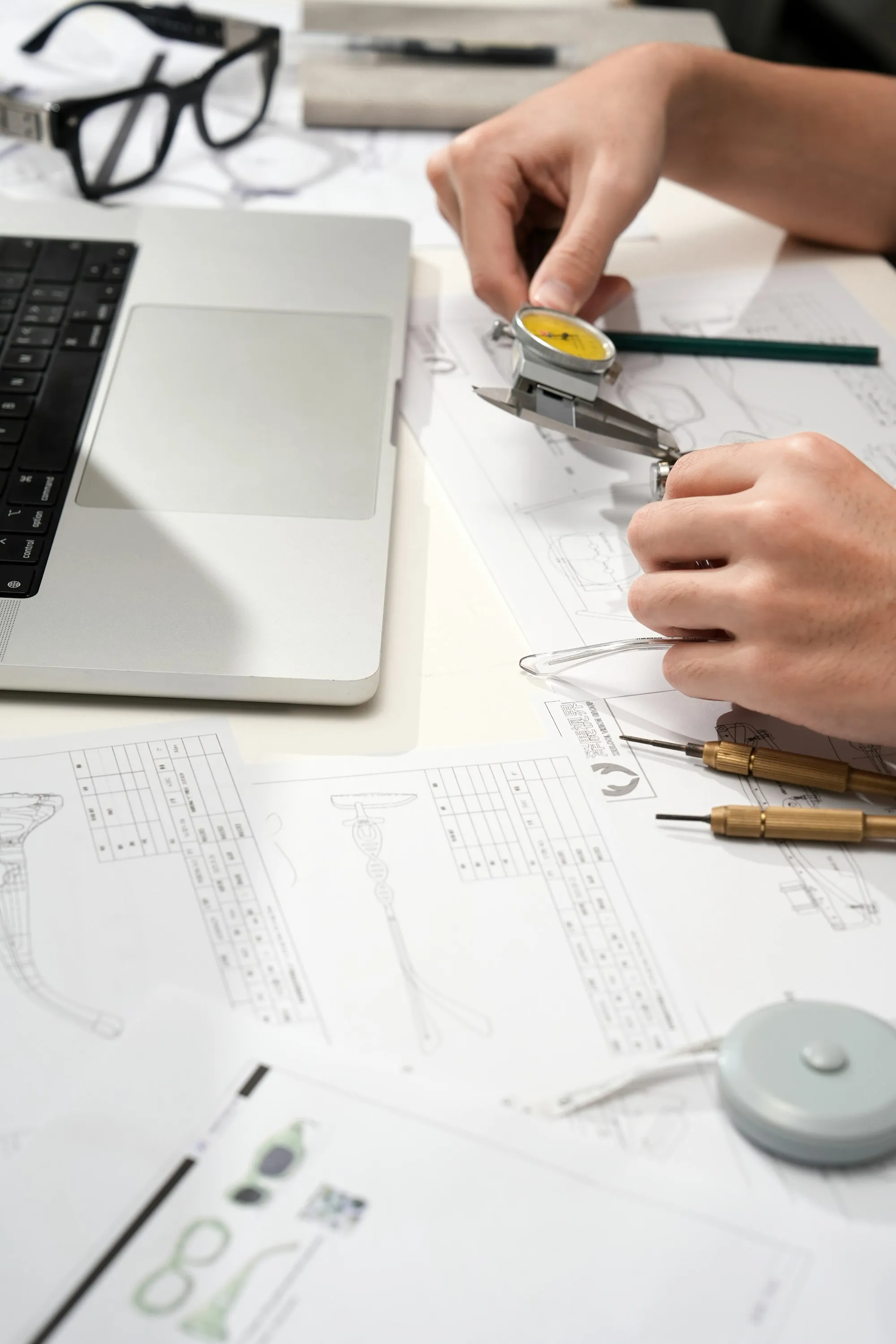 Mão desenhando detalhes técnicos em papel ao lado de um notebook