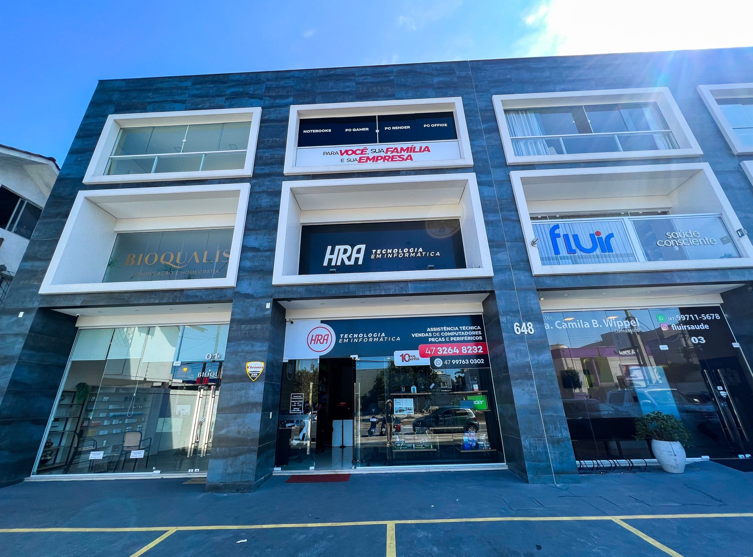 Fachada da HRA Informática: prédio de pastilhas escuras com o letreiro HRA Tecnologia em Informática na vitrine
