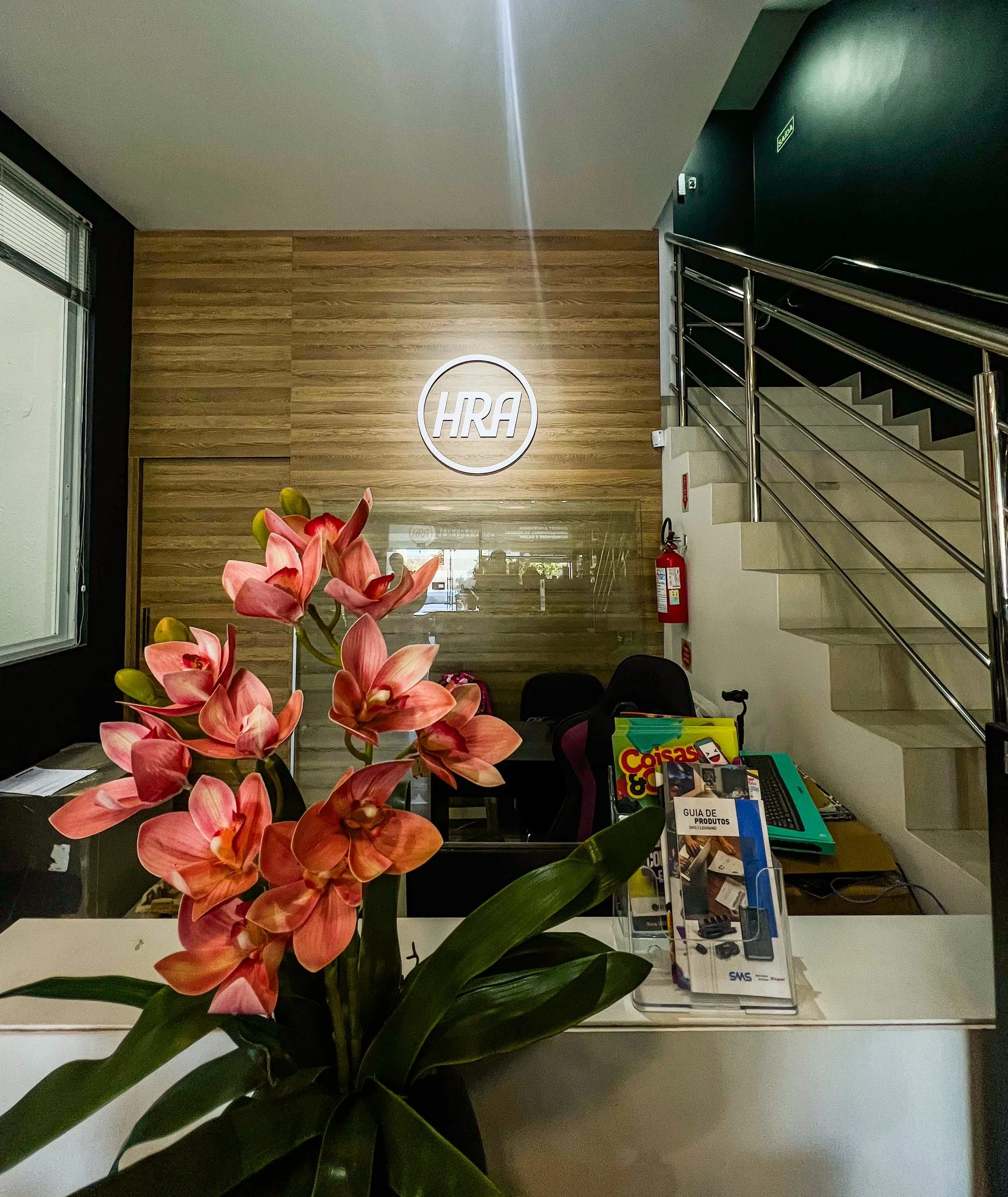 Recepção da HRA, com balcão, orquídeas e a marca na parede de madeira